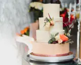 Czteropiętrowy tort weselny w pastelowych kolorach, ozdobiony świeżymi kwiatami i złotym pierścieniem. To najmodniejsze najpiękniejsze torty weselne.