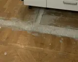 Arbete pågår för att ta bort laminatgolv. Ett vitt pulver och grått material syns på det gamla trägolvet.