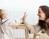 Opiekunka i dziecko dają sobie piątkę nad drewnianym stolikiem.