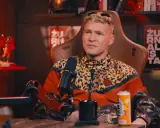 Mężczyzna w kurtce w panterkę, z blond włosami, siedzi w fotelu. Na półce za nim figurki Iron Mana. Wiek majora SPZ.