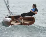 Un homme navigue sur un petit bateau en bois, le "ZUT IV", dans une mer agitée.