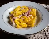 Tortelli ripieni in salsa cremosa con prosciutto, un classico tra i piatti tipici di Parma, serviti in un piatto bianco bordato d'oro.