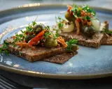 Två bitar mörkt bröd med leverpastej, toppade med cornichoner, chili och krispiga topping. Ett enkelt leverpastej recept att inspireras av.