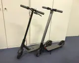 Deux trottinettes électriques, noires et grises, prêtes à l'emploi. La trottinette électrique définition : un moyen de transport urbain pratique.