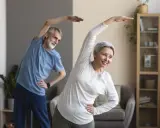 Uśmiechnięta para seniorów ćwiczy w domu. Aktywne zajęcia dla seniorów to świetny sposób na zdrowie i dobre samopoczucie.