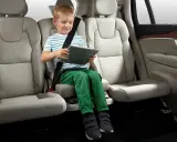 Niño en asiento elevador integrado, con cinturón de seguridad puesto, usando una tablet. ¿Cuál es el asiento más seguro del coche?
