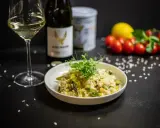 Aksamitne risotto z kurczakiem i szparagami, udekorowane kiełkami. Obok kieliszek białego wina i butelka.
