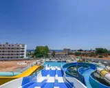 Kolorowe zjeżdżalnie wodne i baseny w Narcissos Waterpark Resort, z hotelami i morzem w tle.