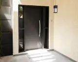 Nowoczesne, ciemnoszare drzwi zewnętrzne otwierane do środka, z bocznymi przeszkleniami i elegancką klamką.