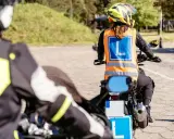 Rozpoczyna się kurs na motocykl. Uczestnicy w kamizelkach z literą "L" ćwiczą jazdę na placu manewrowym.