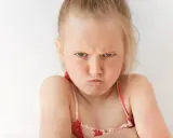 Zagniewane 3 letnie dziecko z zaciśniętymi ustami i skrzyżowanymi rękami.