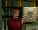Mężczyzna w czerwonej bluzie trzyma okładkę płyty z rysunkiem małpy w słuchawkach, która wygląda jakby słuchała małpa rap.