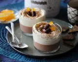 Deux verrines 3 chocolat, garnies de crème fouettée, de copeaux de chocolat et d'écorces d'orange confites.