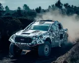 Un Ford Raptor Dakar camuflado levanta polvo en un terreno agreste.