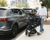 Hombre empuja un cochecito con un sistema sujeción infantil silla coche, junto a un coche gris.