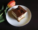 Pyszny kawałek tiramisu, jednego z 10 ciast bez pieczenia, obok czerwonego tulipana.