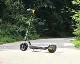 Trottinette Xiaomi grise sur une route asphaltée, entourée de verdure. Parfait pour explorer la nature et profiter de son autonomie.