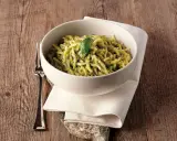 Un piatto invitante di trofie al pesto, guarnito con una foglia di basilico, su un tavolo di legno rustico.