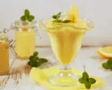 Pyszny lemon curd przepis w pucharku, ozdobiony cytryną i miętą. Obok słoiczki z kremem.