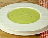 Una ciotola di cremosa crema di zucchine, condita con pepe nero, servita su piatti bianchi su un tavolo di legno.