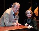 La signora Frola e il signor Ponza, suo genero, si guardano con espressione preoccupata, appoggiati a un tavolo di legno scuro.