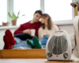 Pareja acurrucada con bebidas calientes, un radiador eléctrico en primer plano. Así funciona un radiador eléctrico para calentar el hogar.