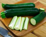 Courgettes vertes entières et coupées en bâtonnets sur une planche à découper, prêtes à congeler.