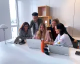 Zespół młodych ludzi pracuje razem przy biurku w biurze Alstom Wrocław, śmiejąc się i patrząc na ekran laptopa.