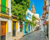 Calle empedrada con casas blancas adornadas con flores y enredaderas. Al fondo, la torre de la Mezquita-Catedral, un imprescindible que ver en Andalucía.