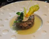 Un tartare de poisson finement préparé, garni de crème, herbes fraîches et d'une fleur jaune, une des spécialités Limoges.