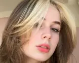 Dziewczyna z burzą blond i brązowych włosów w stylu curly wolf cut, z pasemkami przy twarzy.