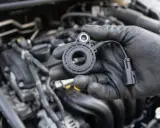 Mechanik w czarnej rękawiczce trzyma czujnik spalania stukowego, gotowy do montażu w silniku samochodu.