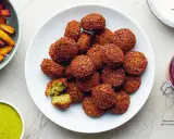 Talerz pełen chrupiących kuleczek, które są idealnym przykładem tego, co to jest falafel. Podane z zielonym sosem i frytkami.