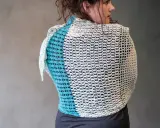 Mujer de espaldas con un cubre hombros a crochet de dos colores, blanco y azul turquesa, con un diseño calado.