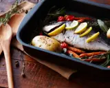 Pescado al horno con patatas, zanahorias y tomates, listo para servir.