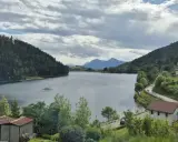 Panoramica del lago di Stramentizzo circondato da montagne verdi e un villaggio pittoresco. Nuvole minacciose nel cielo.