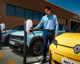 Un homme charge une automobile hybride électrique turquoise. Une voiture jaune est garée à côté.