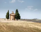 Cappella della Madonna di Vitaleta, icona della Val d'Orcia, circondata da cipressi e dolci colline toscane sotto un cielo azzurro.