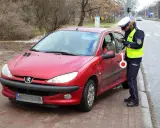 Policjantka w kamizelce odblaskowej i czapce spisuje kierowcę przy czerwonym samochodzie.
