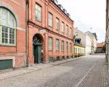Gammalt tegelhus med gröna fönster och dörrar, en del av ett charmigt vandrarhem i Skåne. Gatsten leder längs en lugn gata.