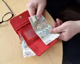 Ręce wkładają banknot 500 zł do czerwonego portfela. Obok okulary. Może to być pomocne przy sprawdzaniu 14 emerytury tabeli netto.