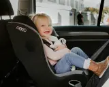 Uśmiechnięta dziewczynka w foteliku rwf, przytulająca pluszową zabawkę, bezpiecznie podróżuje samochodem.