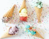 Cinco conos de helado de chuche de colores vibrantes, esparcidos con confeti sobre fondo blanco.