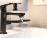 Robinet noir moderne, eau claire coulant dans un lavabo. Un adoucisseur d'eau est peut-être installé pour lutter contre l'eau calcaire.