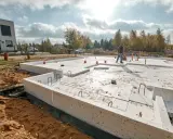 Budowa domu w toku. Widoczne różne rodzaje fundamentów, w tym płyta fundamentowa i ławy fundamentowe, przygotowane do dalszych prac.