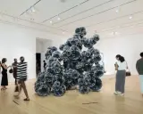 Visitors admire a large, dark, spherical sculpture in a bright gallery space, typical of Indianapolis Museum of Art photos.