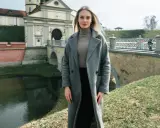 Kobieta w szarym płaszczu i golfie, idealna stylizacja na 14 stopni. W tle zamek i most.