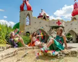 Trzy dziewczynki w strojach wróżek siedzą nad wodą przed bajkowym zamkiem. To jedne z wielu magiczne ogrody atrakcje.