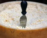 Ein Parmesanrad mit einem Messer, bereit zum Portionieren. Der Unterschied zwischen Parmesan und Pecorino ist oft im Geschmack und der Textur zu finden.