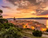 Sonnenuntergang über St. Tropez. Die Sonne versinkt im Meer, beleuchtet die Stadt und den Kirchturm in warmen Farben.